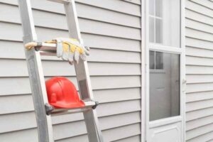 Red hard hat and work gloves on a ladder with house siding background.