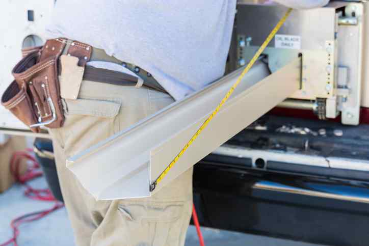 Worker Measuring An Aluminum Rain Gutter Feeding Through Seamless Shaping Machine.